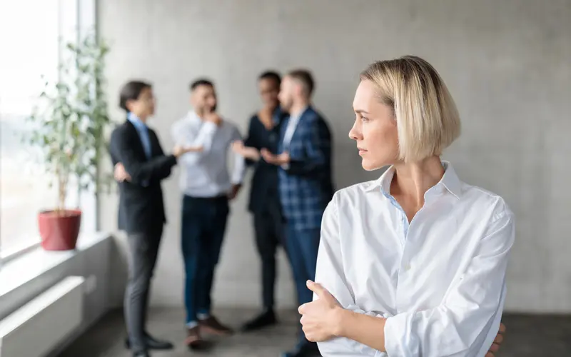 An unhappy female office worker with men whispering to each other behind her