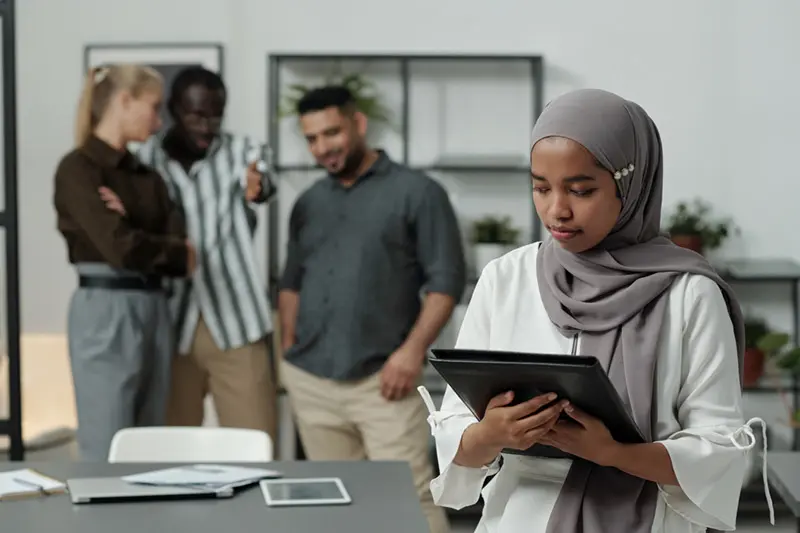 A young Muslim woman in the office with people whispering behind her back