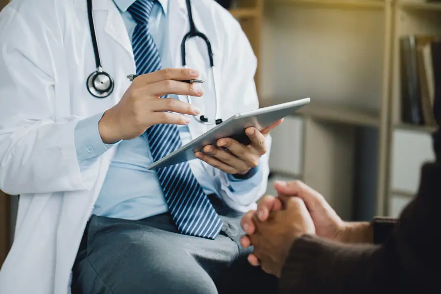 A doctor in a white coat with stethoscope talking to a patient