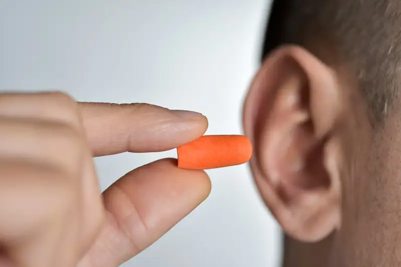A man inserting an orange disposable earplug into his ear