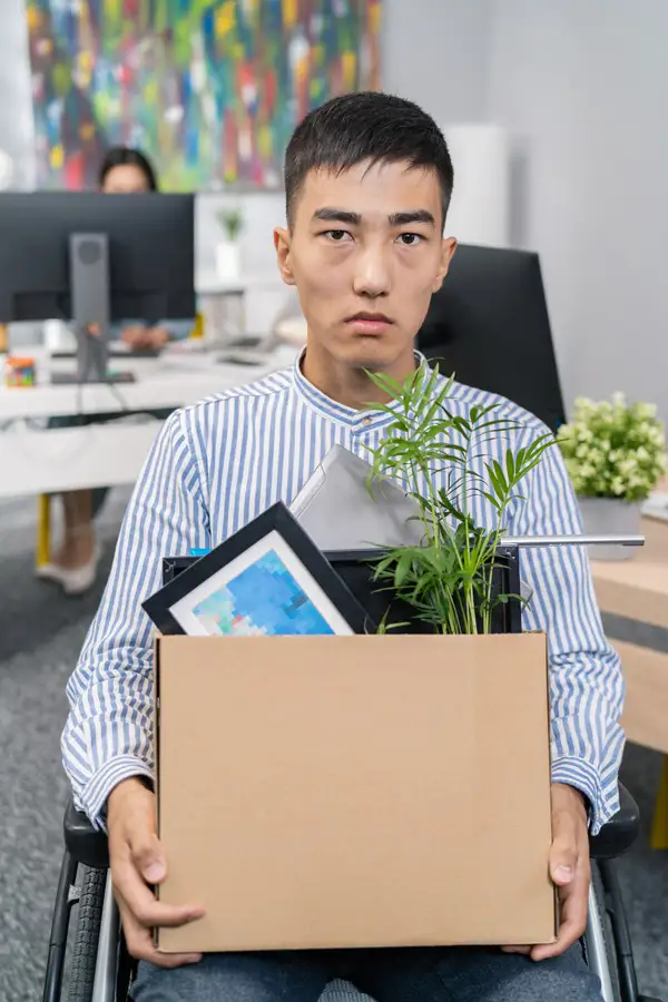 A man in a wheelchair holding his belongings in an office after being fired