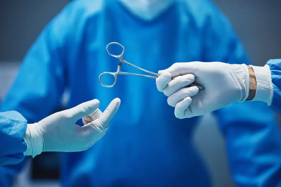 Nurse handing surgical forceps to a surgeon during a surgery