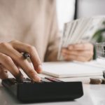 Woman counting and calculate cost money with calculator at home. Budget of disadvantaged and low income family for rising food and grocery store prices and expensive daily consumer goods concept.