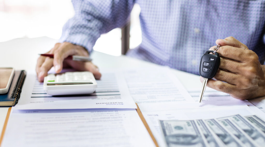 Men's hand holding car key calculate monthly installments and reviewing personal loan contract and car accident insurance before making an agreement about contract to apply for a car loan